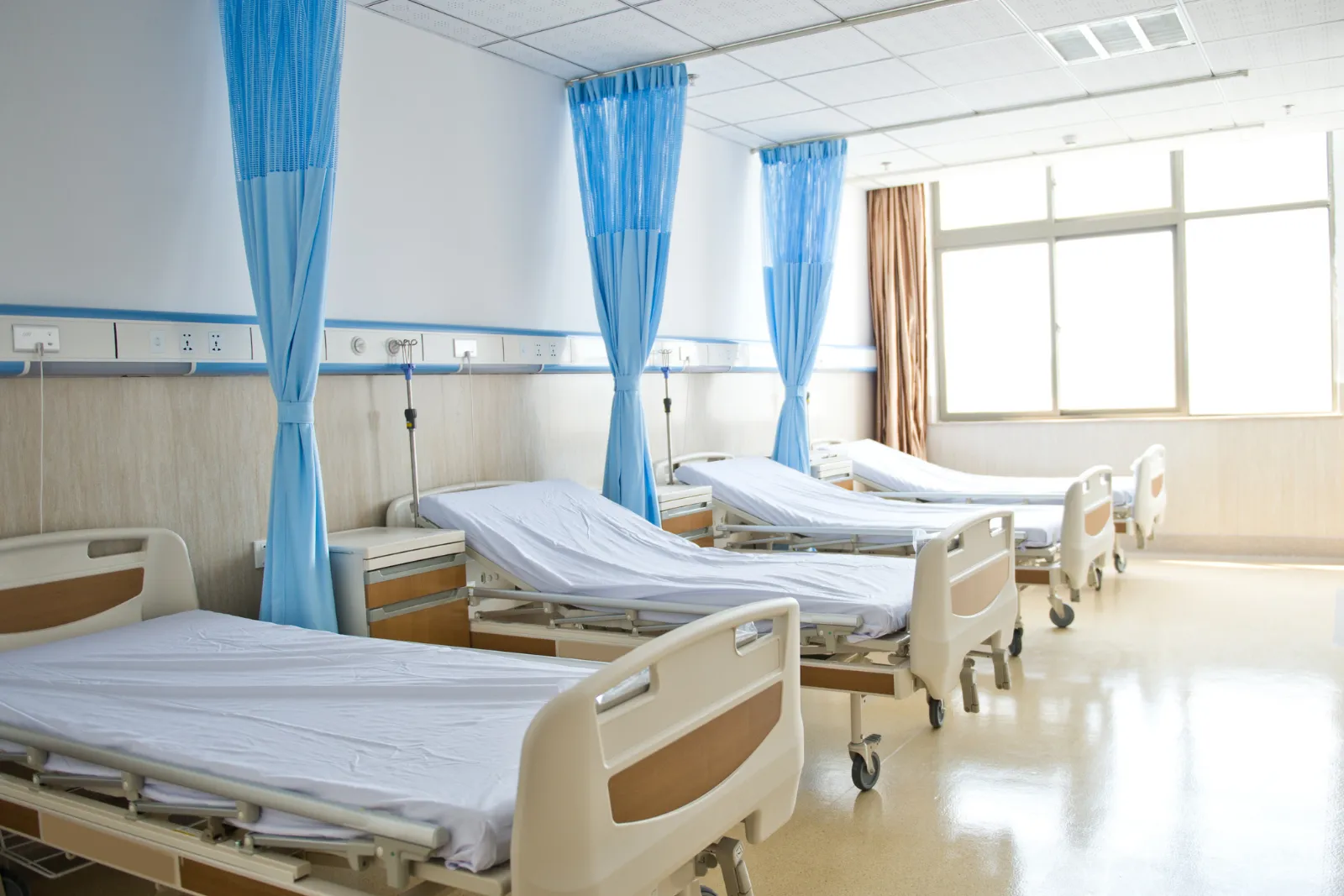 Sala de hospital público con cortinas azules y camas compartidas