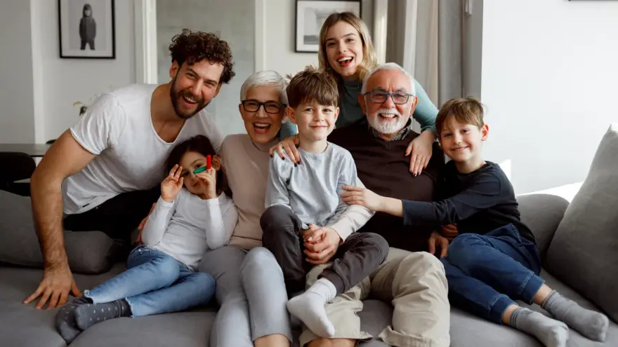 Tres generaciones de una familia sonriendo juntas en la sala de su casa