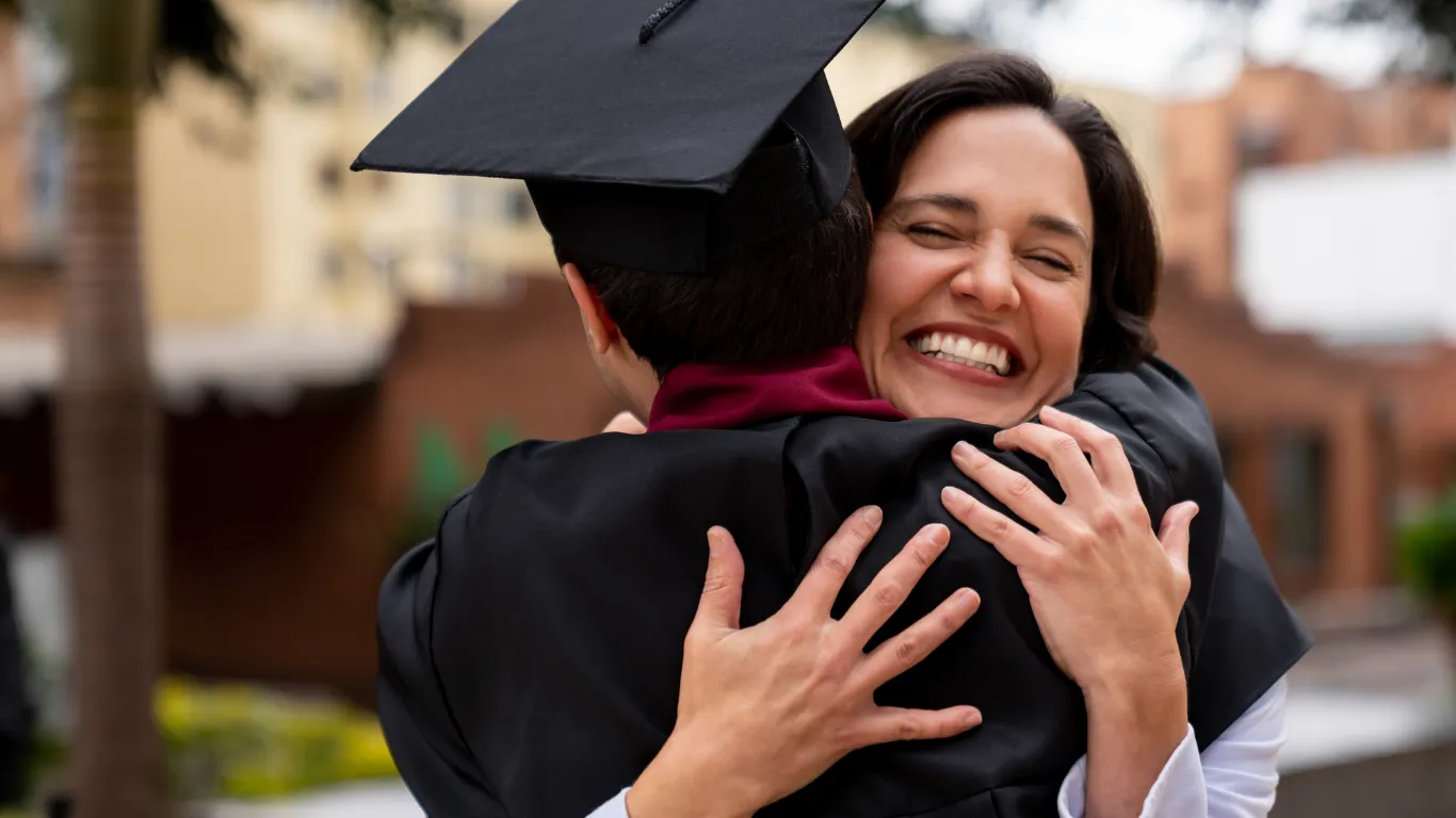 Una madre abraza a su hijo el día de su graduación universitaria — el resultado de años de previsión familiar