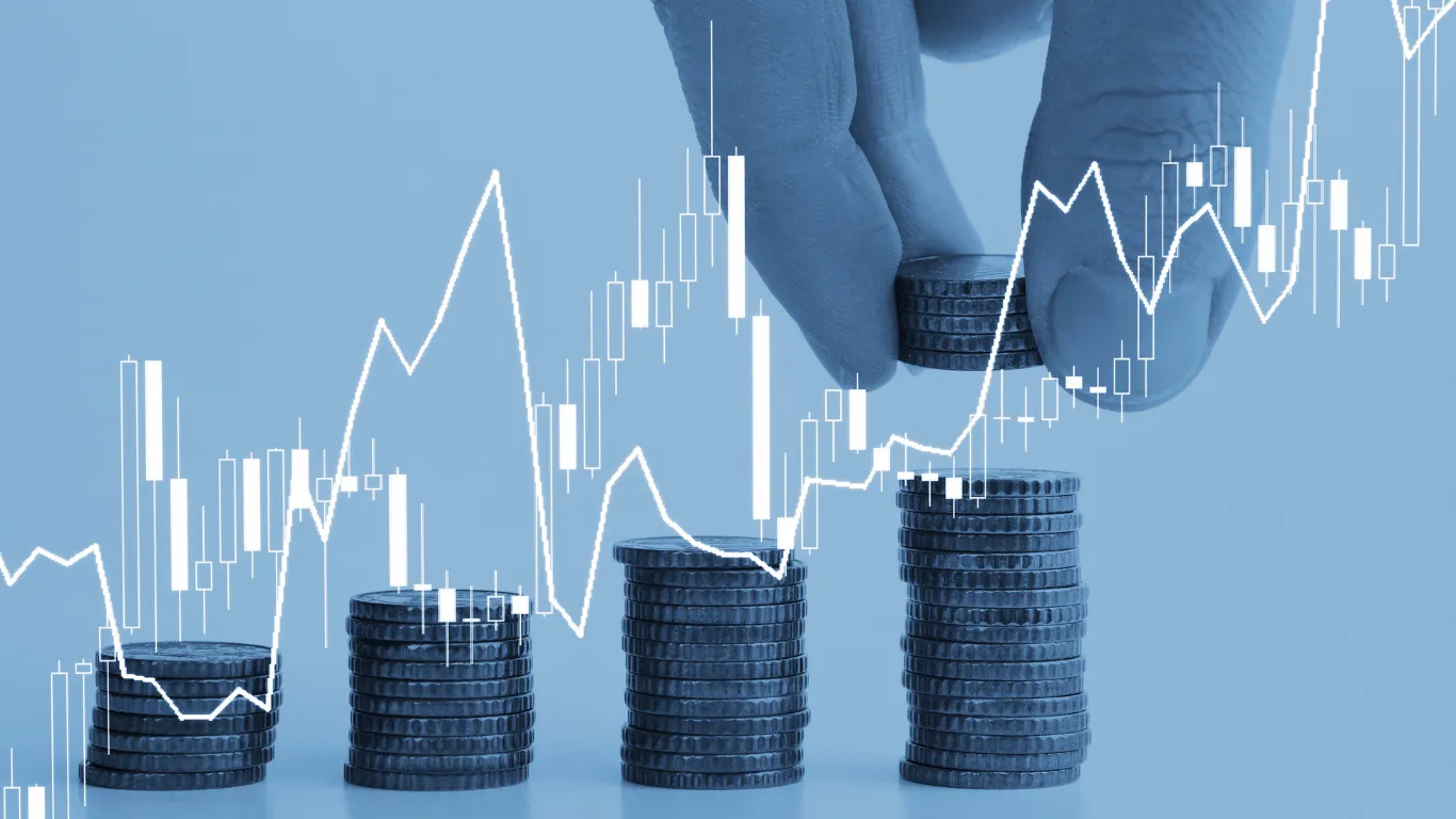 Monedas apiladas en pilas crecientes con una gráfica de rendimiento al alza — el interés compuesto hace crecer cada aportación mes con mes
