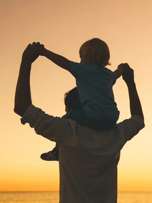 Padre cargando a su hijo en hombros al atardecer en la playa