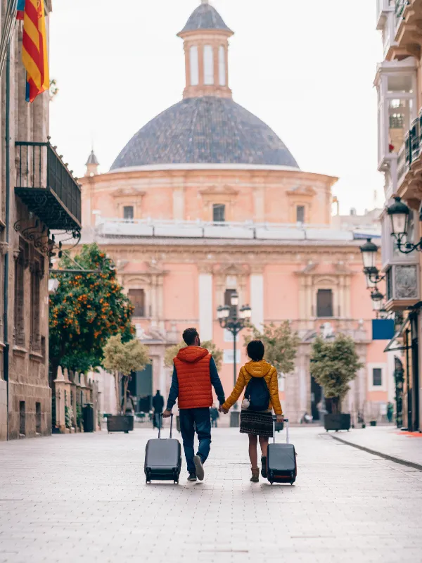 Pareja de mexicanos viajando con maletas en una plaza europea